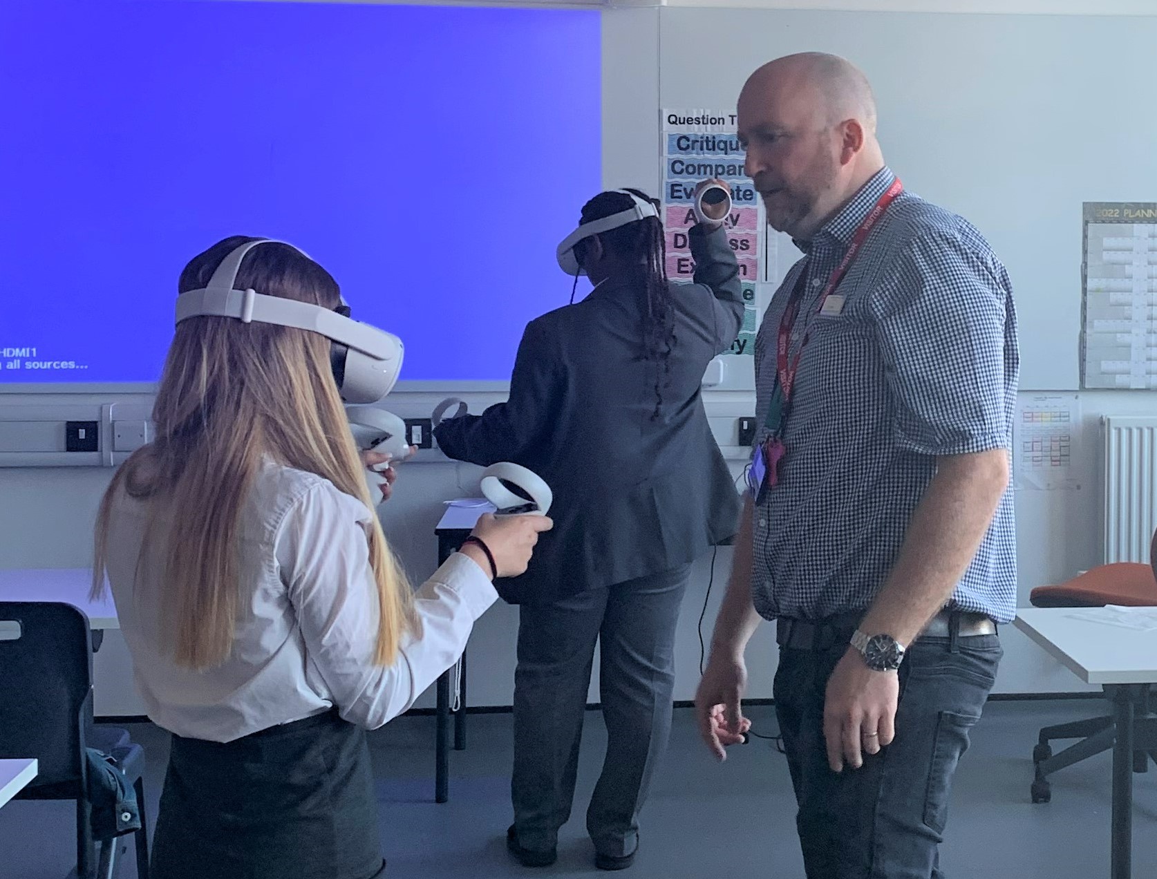 A female student at a University Technical College (UTC) using Virtual Reality (VR) headset with colleague from Sheffield Children's Hospital. In the background there is another student also wearing a VR headset.
