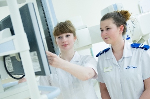 Two young female radiographer students are using an x-ray machine.